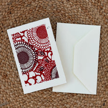 Load image into Gallery viewer, Colby Cards, lifestyle image of a white Lokta paper greeting card featuring a rectangular red and burgundy floral print with large circular blooms, displayed with a white envelope on a brown woven mat.