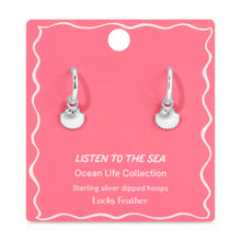 Load image into Gallery viewer, Pair of sterling silver-dipped hoop earrings with small scallop shell charms displayed on a pink &quot;Listen to the Sea&quot; Ocean Life Collection card by Lucky Feather with white wavy border detailing, displayed against a white background. 