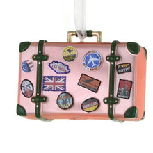 Load image into Gallery viewer, Traveler Luggage Ornament, pink painted glass suitcase ornament with dark green straps and corner accents, gold-colored buckles and handle, colorful travel-sticker illustrations, and a sheer white hanging ribbon, against a white background.