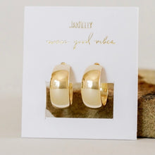 Load image into Gallery viewer, Gold Wide Hoop Earrings, 18K gold-plated, smooth C-shaped hoops with slightly inflated centers and tapered ends, displayed on a white jewelry card with gold "JAXKELLY" and "wear good vibes" lettering against a neutral stone and cream background. 