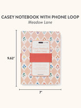 Load image into Gallery viewer, &quot;CASEY NOTEBOOK WITH PHONE LOOP , Meadow Lane&quot; text on a white background. 
A pink and white checkered notebook with different colored flowers in the white checkers. A pink colored cell phone holder in the center of the notebook, and a pink pen holder on the side. Measurements &quot;9.62 x 7&quot; beside the notebook. On a white background. 