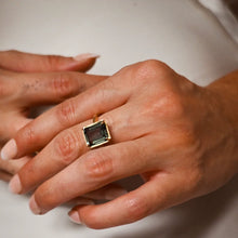 Load image into Gallery viewer, Double gold-plated brass ring with a rectangular emerald-cut green tourmaline spinel stone shown on a person's hand against a soft white background. 