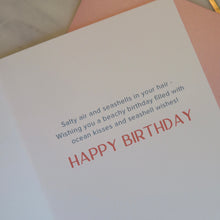 Load image into Gallery viewer, Birthday card with &quot;Salty air and seashells in your hair- Wishing you a beachy birthday filled with ocean kisses and seashell wishes! HAPPY BIRTHDAY&quot; text with pink envelope on a marble background.