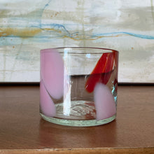 Load image into Gallery viewer, Splash Cup clear hand-blown glass with abstract light pink and red swirled design on wooden surface against abstract background. 
