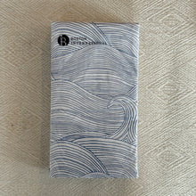 Load image into Gallery viewer, Folded paper guest napkins featuring blue wave pattern on white background, displayed on woven neutral surface.