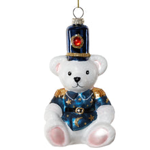 Load image into Gallery viewer, Teddy Bear Glass Ornament, front view of a seated white bear glass ornament with pale pink ears and paw pads wearing a metallic blue uniform decorated with gold stars and a crescent moon, gold shoulder accents, a black belt, gold glitter accents, and a tall blue hat with a red jewel-like accent against a white background.