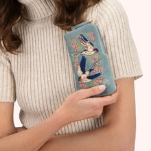 Load image into Gallery viewer, Person wearing a cream ribbed turtleneck sweater holding a light blue velvet zippered sunglass pouch with embroidered blue and white swallows and pink floral designs. Against a white background. 