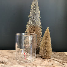 Load image into Gallery viewer, A glass tumbler with a red and white striped candy cane design , next to two frosted decorative Christmas trees. Tumbler and trees are on a cream and brown marble slab. Against a blue background. 