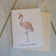 Load image into Gallery viewer, Greeting card with a flamingo illustration and &quot;You&#39;re one of a kind&quot; text with a beige envelope on a marble surface
