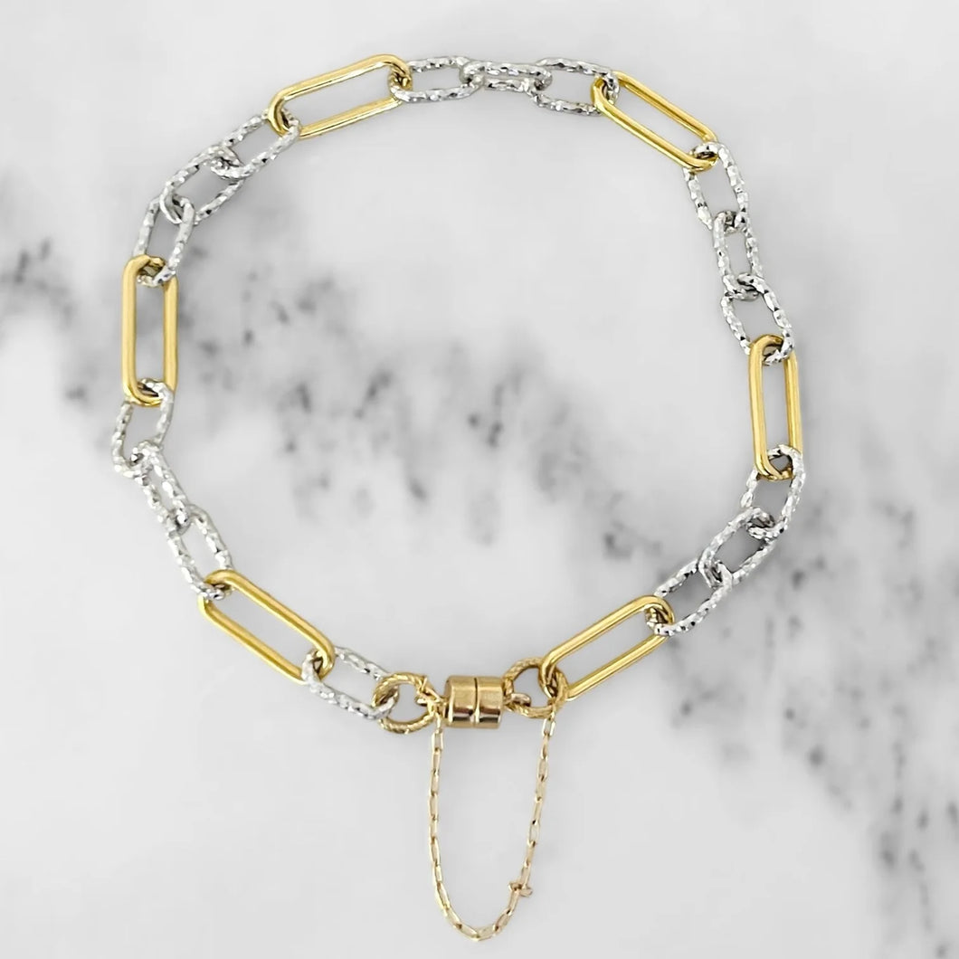 Alternating gold and hammered silver paperclip chain bracelet with a magnetic clasp. White marble background. 