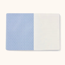 Load image into Gallery viewer, A notebook opened showing the inside of the cover in dark and light blue, and the first lined paged . On a white background.