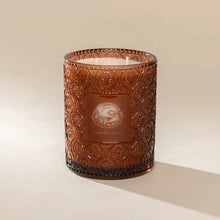 Load image into Gallery viewer, Poured NY Curiositeas Candle | Two Styles, candle with white wax and a double unlit wick in a cylindrical translucent rust-colored glass vessel with an all over ornate embossed geometric pattern and smooth matching label featuring a white teacup illustration against a cream background. 