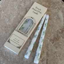 Load image into Gallery viewer, Two white taper candles with blue-and-green floral designs on a brown marble surface, next to their packaging.  