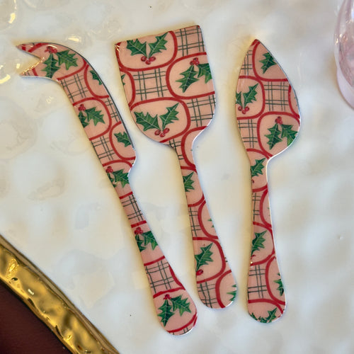 Set of three white enameled stainless steel servers with a festive mistletoe design in red and green. On top of a white surface with a gold border.