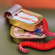 Load image into Gallery viewer, Two tin cans resembling tinned fish. Top tin is opened exposing a candle shaped like octopuses. Bottom tin is unopened. Large ,red, octopus tentacle draping over tins. 