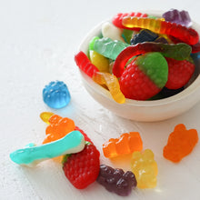 Load image into Gallery viewer, Assorted gummy candies including worms, strawberries, and bears in a small bowl with candies scattered on a white surface. 