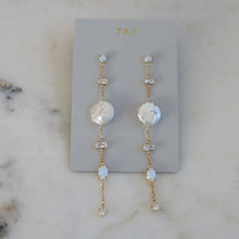 Load image into Gallery viewer, Gold-plated baroque style duster earrings with clear baguette stones on a light gray TAI jewelry card displayed on a white marble background.