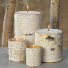 Load image into Gallery viewer, Assorted lit birch-wrapped candles displayed on a gray surface against a neutral background with birch branches. 