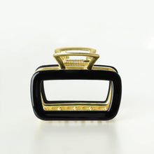 Load image into Gallery viewer, Black rectangular metal claw clip with gold hardware displayed on a white background. 