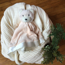 Load image into Gallery viewer, Peach colored plushie with a  teddy bear head cradled on white muslin blanket, wooden background with greenery. 