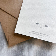 Load image into Gallery viewer, Back of the hand-painted card on textured white paper with small black printed branding text, displayed with a kraft paper envelope on a textured light gray fabric surface. 
