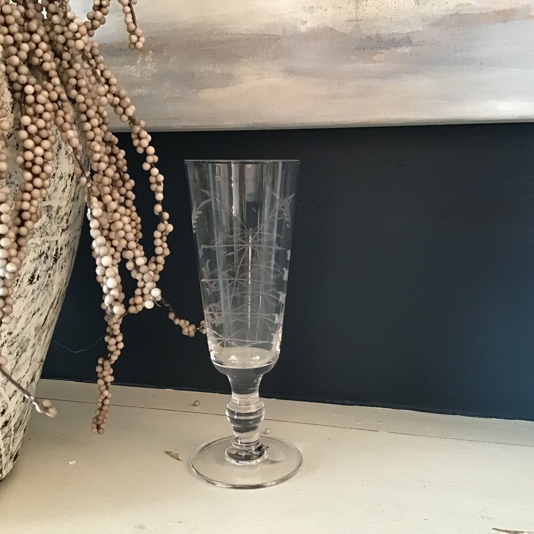 Clear flute glass with engraved designs against dark background 