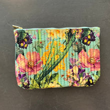 Load image into Gallery viewer, Quilted velvet zip pouch featuring a multicolor spring floral pattern with pink, yellow, and purple flowers on a light turquoise background and top zipper closure, displayed on a dark surface. 