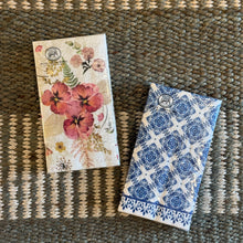 Load image into Gallery viewer, Michel Design Works Pressed Flowers and Indigo Seas hostess napkins in packaging, displayed side by side on a woven surface, featuring red and pink floral and blue tile-inspired patterns. 
