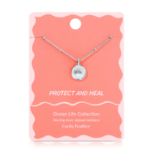 Load image into Gallery viewer, Sterling silver-dipped necklace featuring a small scallop shell charm pendant and a chain with delicate beaded accents, displayed on a light pink &quot;Protect and Heal&quot; Ocean Life Collection card by Lucky Feather with a white wavy border against a white background. 