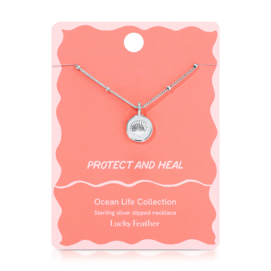 Sterling silver-dipped necklace featuring a small scallop shell charm pendant and a chain with delicate beaded accents, displayed on a light pink 