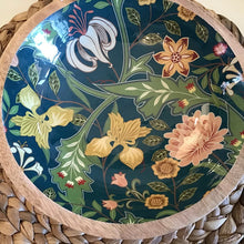 Load image into Gallery viewer, An enamel bowl in a dark green ,pink, yellow, and light green floral design , on a woven background.