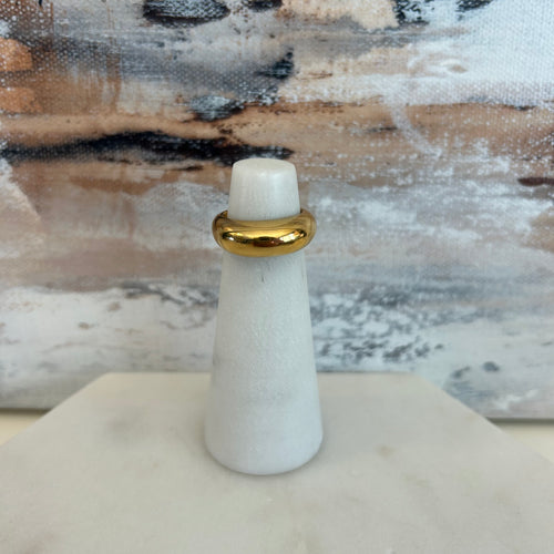 Thick gold ring on a marble stand with a neutral abstract painting as the background. 