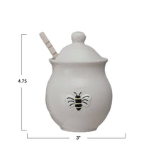 Load image into Gallery viewer, A white honey jar with a bee design, lid, and a wooden spoon . Measurements 4.75&quot; X 3&quot; . On a white background. 