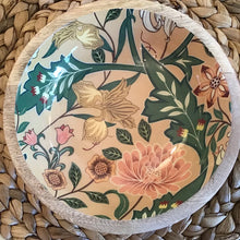 Load image into Gallery viewer, A decorative enamel bowl with a floral pattern in beige, pink, and green. On a woven background.