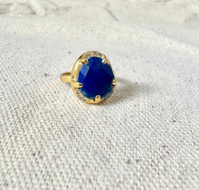 Load image into Gallery viewer, Double-gold-plated brass ring featuring an oval blue lapis stone in a prong setting with small CZ accent stones along the base, displayed on a light textured surface.   