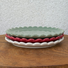 Load image into Gallery viewer, Green, red, and white stacked  ceramic plates with scalloped edges on a brown wooden surface , against a white textured background.
