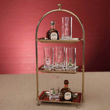 Load image into Gallery viewer, ZODAX Holiday Shot Glasses, lifestyle image of tall clear shot glasses with thick bases and raised Santa, Christmas tree, and red-and-white candy cane motifs, arranged with miniature liquor bottles on a three-tier gold-tone stand against a red background.