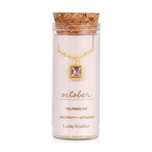 Load image into Gallery viewer, October birthstone necklace featuring a square light-pink tourmaline glass crystal pendant framed in 14K gold-dipped metal, displayed inside a clear glass bottle with a cork lid and a label card reading "October - Tourmaline - Creativity + Optimism," displayed against a white background.
