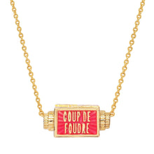 Load image into Gallery viewer, Close-up of the gold-plated rectangular spinner pendant necklace with red enamel featuring the words "COUP DE FOUDRE," suspended on a gold-plated chain displayed on a white background. 