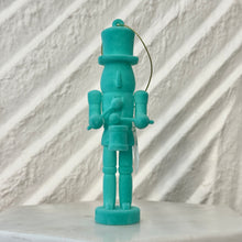 Load image into Gallery viewer, Teal nutcracker ornament holding a small drum and drumsticks, standing upright with a gold hanging cord against a white textured background. 
