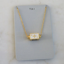 Load image into Gallery viewer, Close-up of a gold-plated spinner pendant chain necklace with a white enamel starburst design on a light gray TAI card, displayed on a white background. 