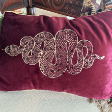 Load image into Gallery viewer, Beaded Snake Lumbar Pillow, burgundy velvet lumbar pillow with printed and beaded gold snake design and gold piping along edges, on a textured surface. 