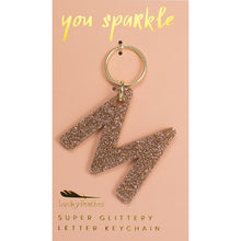 Load image into Gallery viewer, Gold glittery letter &quot;M&quot; keychain on a pink card with &quot;you sparkle&quot; in gold text, displayed against a white background.