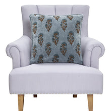 Load image into Gallery viewer, Dusty blue velvet throw pillow with a Mughal floral pattern displayed on a light upholstered armchair against a white background. 