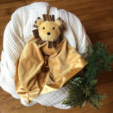 Load image into Gallery viewer, Brown plushie blanket with a lion head swaddled in a white muslin blanket, wooden background with greenery. 