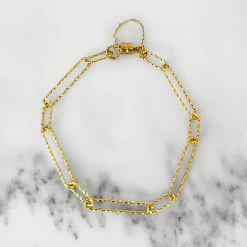 Hammered gold paperclip chain bracelet with a magnetic clasp. White marble background. 