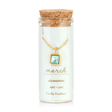 Load image into Gallery viewer, March birthstone necklace featuring a square aquamarine-colored glass crystal pendant framed in 14K gold-dipped metal, displayed inside a clear glass bottle with a cork lid and a label card reading "March - Aquamarine - Hope + Love," displayed against a white background. 