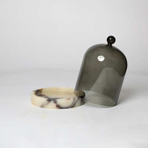 A black glass cloche with a cream and black marble base, displayed on a white background.
