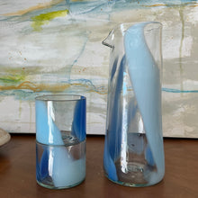 Load image into Gallery viewer, Splash Cup clear hand-blown glass with abstract blue and light blue swirled design, stacked on one another beside a matching pitcher on wooden surface against an abstract background. 