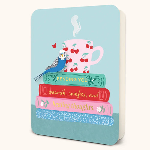 Blue greeting card featuring an illustration of a blue and white parakeet perched on a stack of three books- green, red, pink, and  blue with white swirls- with the message 